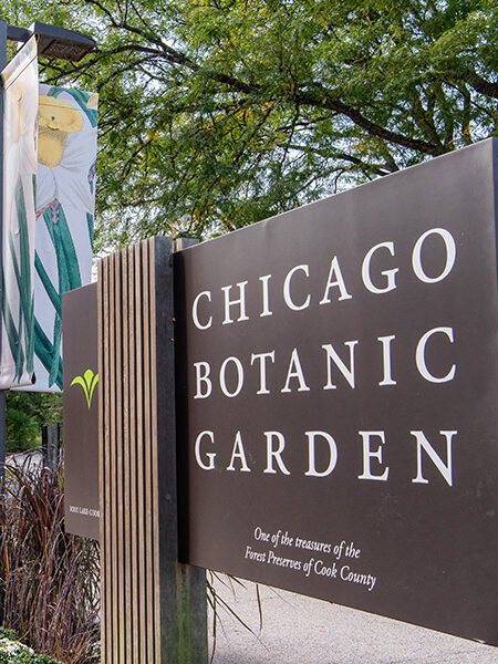 Entrance signs for the Chicago Botanic Garden, with a banner advertising the Fall Bulb Festival from October 9 to 11. Trees and plants are visible in the background.