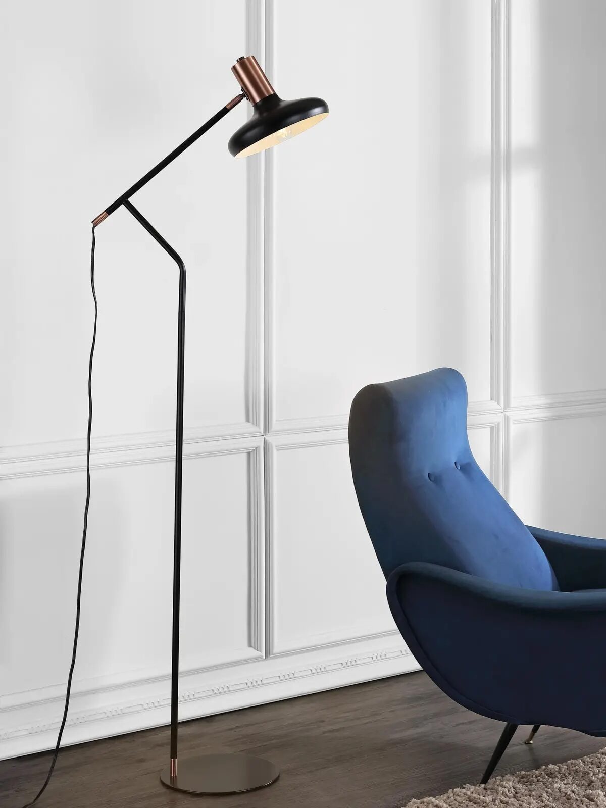A modern blue armchair sits next to a black floor lamp in a room with white paneled walls and a textured beige rug.