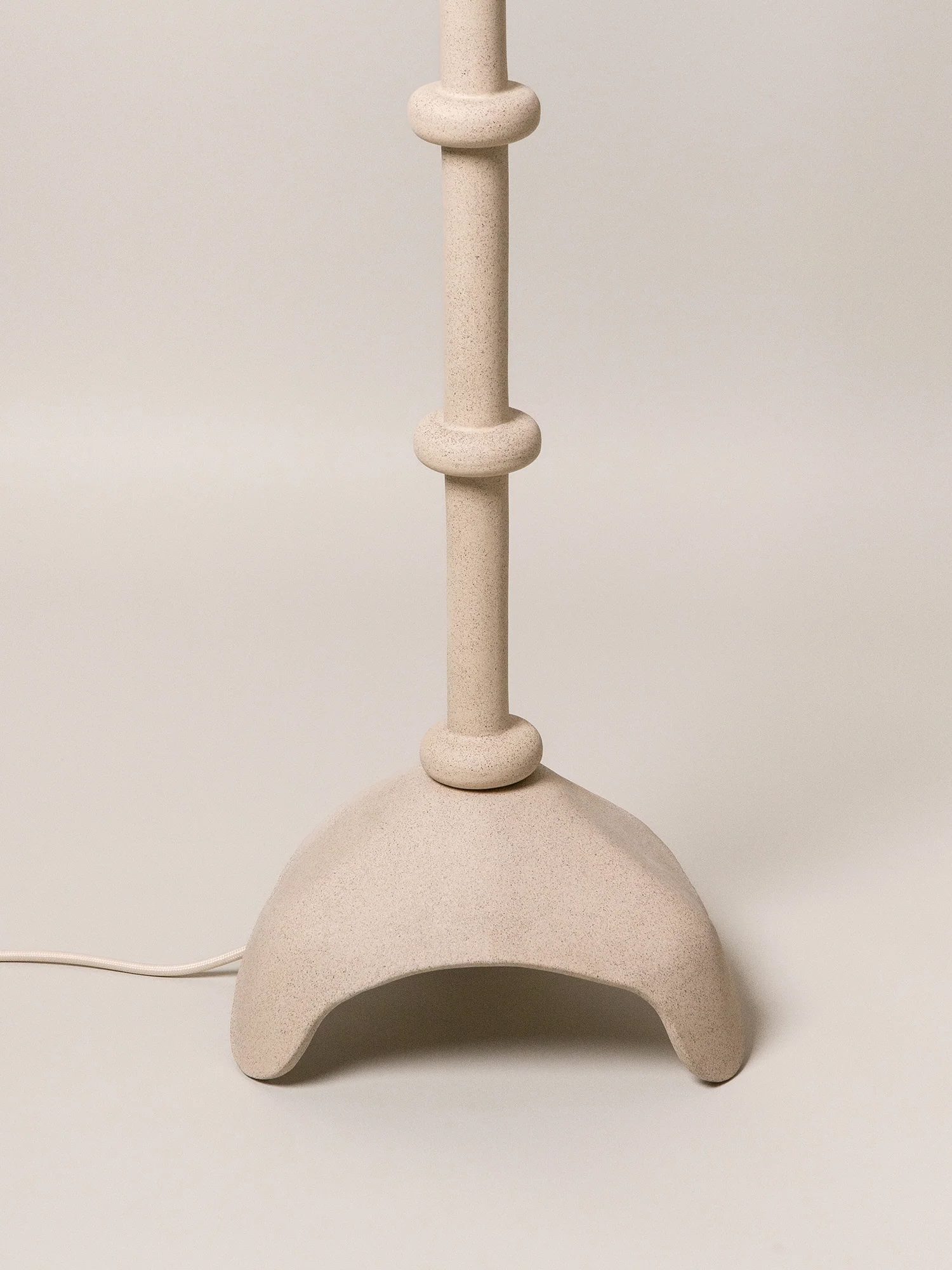 Beige sculptural lamp base with rounded details and a curved, three-legged design, shown against a plain background with a visible power cord.