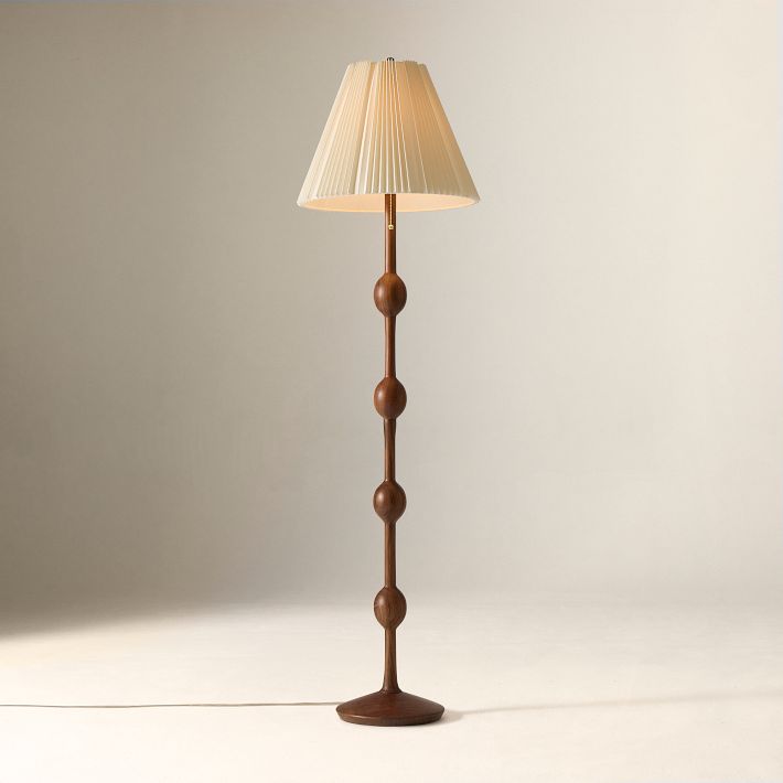 A tall floor lamp with a pleated cream lampshade and a brown wooden base featuring four spherical accents, set against a plain background.