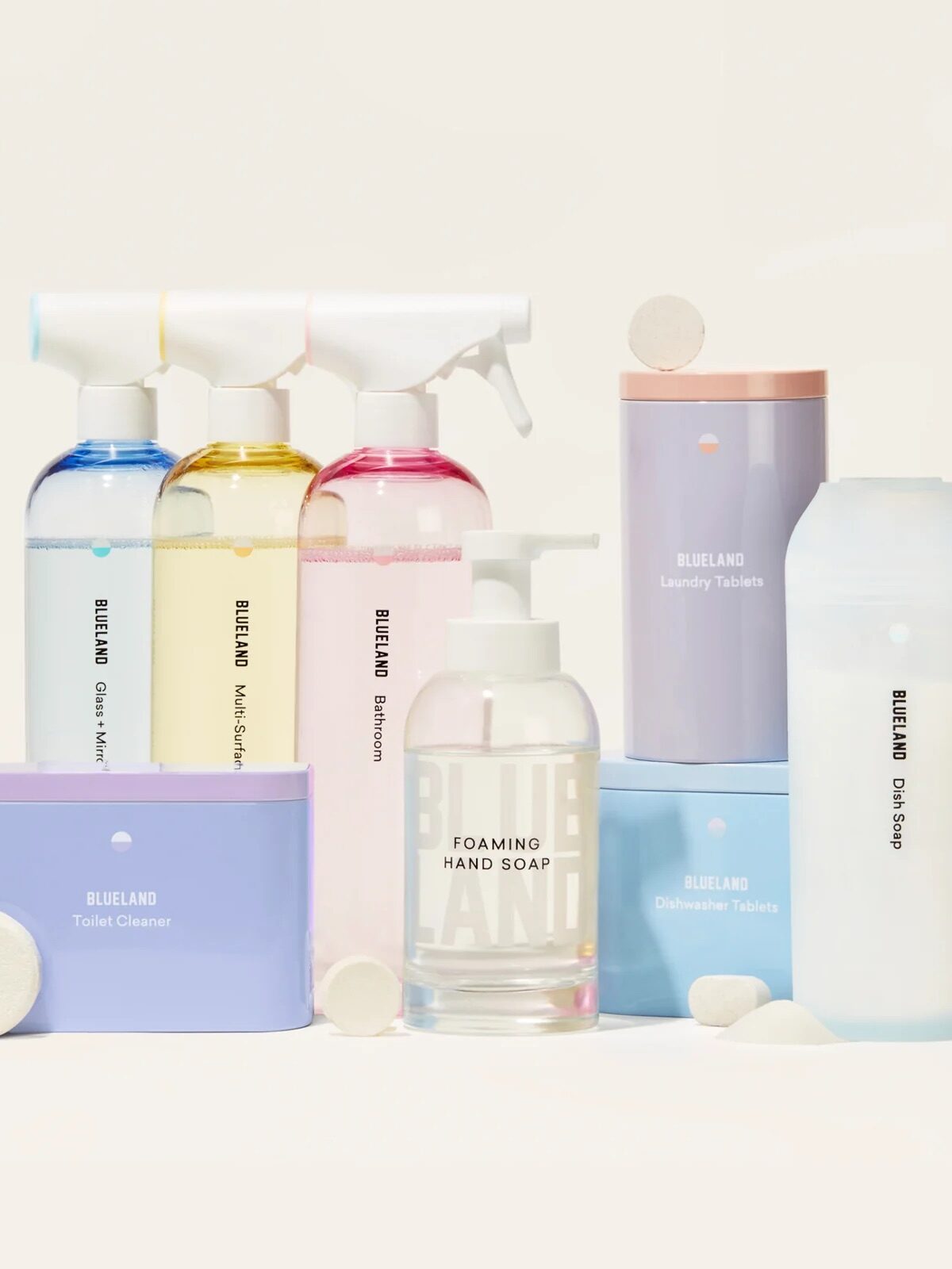 A variety of BLUELAND cleaning and soap products, including spray bottles, soap tablets, a foaming hand soap dispenser, and containers, are arranged on a light surface.