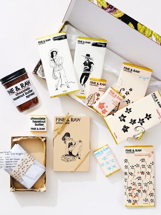 A selection of Fine & Raw chocolate bars with illustrated wrappers, a jar of chocolate hazelnut spread, and a note, all arranged on a white surface.