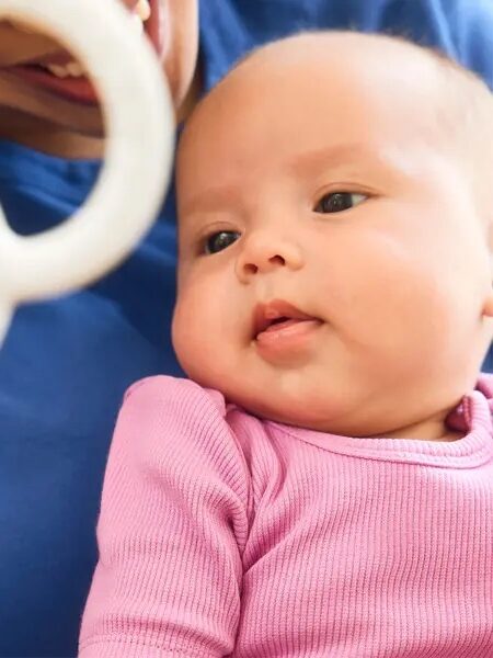 A baby in a pink outfit looks at a black and white rattle held by an adult, with a label pointing to the rattle that reads "Trackable sounds.