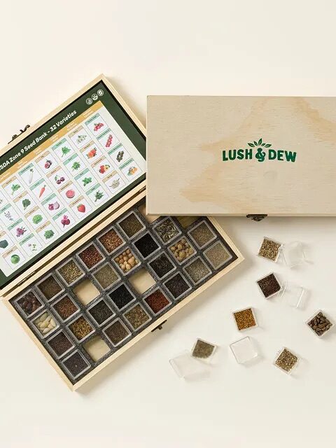 A wooden Lush & Dew box open to display 32 small containers of seeds and an illustrated chart of plant varieties; box lid with logo rests beside it.