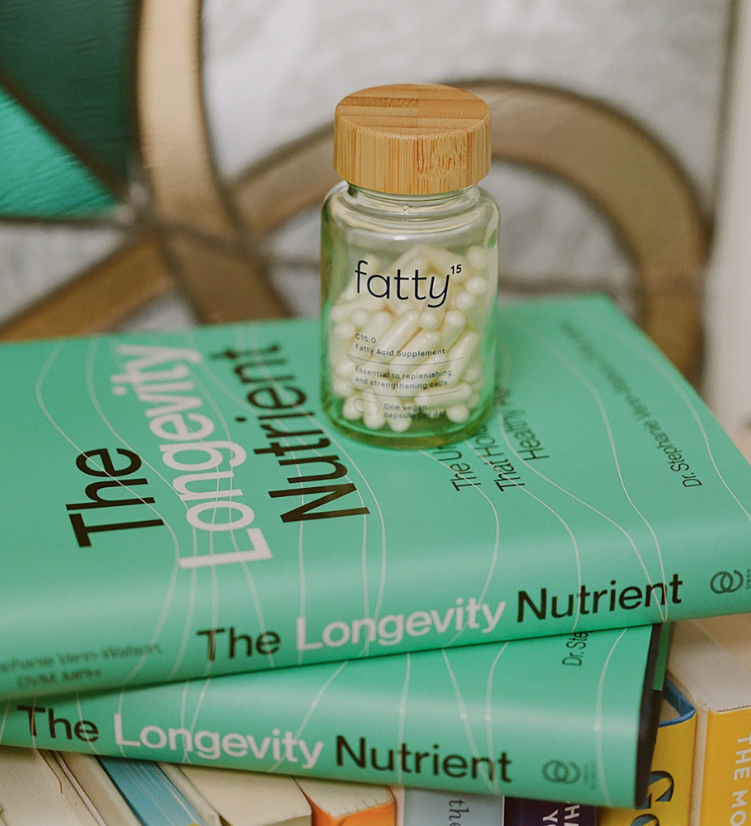 A bottle labeled "fatty15" with white capsules is placed on top of two green books titled "The Longevity Nutrient.