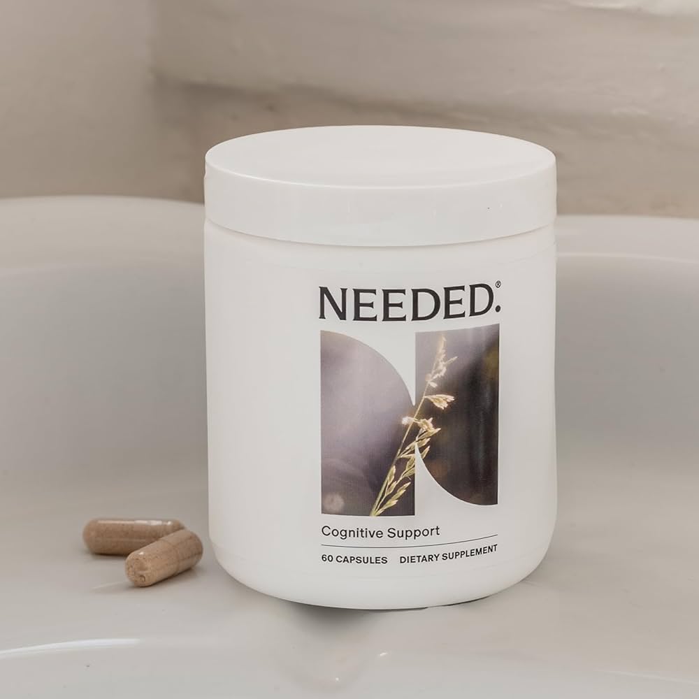 A white container labeled "Needed: Cognitive Support" with two brown capsules beside it, placed on a light-colored surface.
