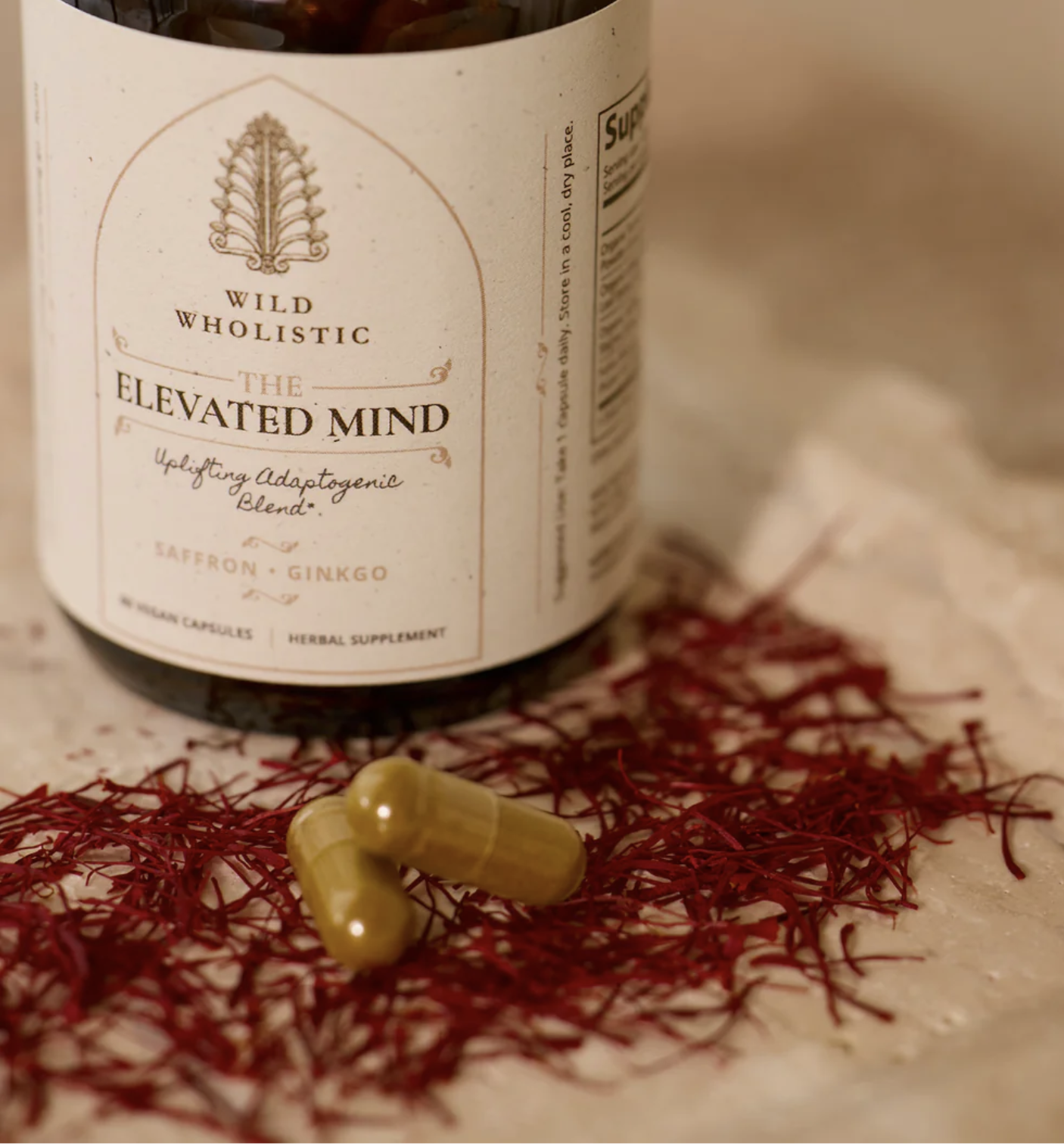 A bottle labeled "The Elevated Mind" herbal supplement sits on a surface with saffron threads and two green capsules nearby.