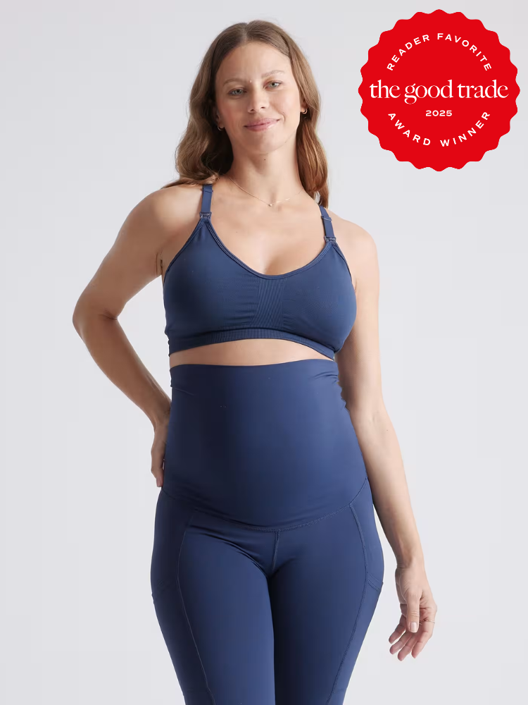 A woman wearing a navy blue sports bra and high-waisted leggings stands against a plain background. A red badge reads “The Good Trade 2025 Award Winner Reader Favorite.”.