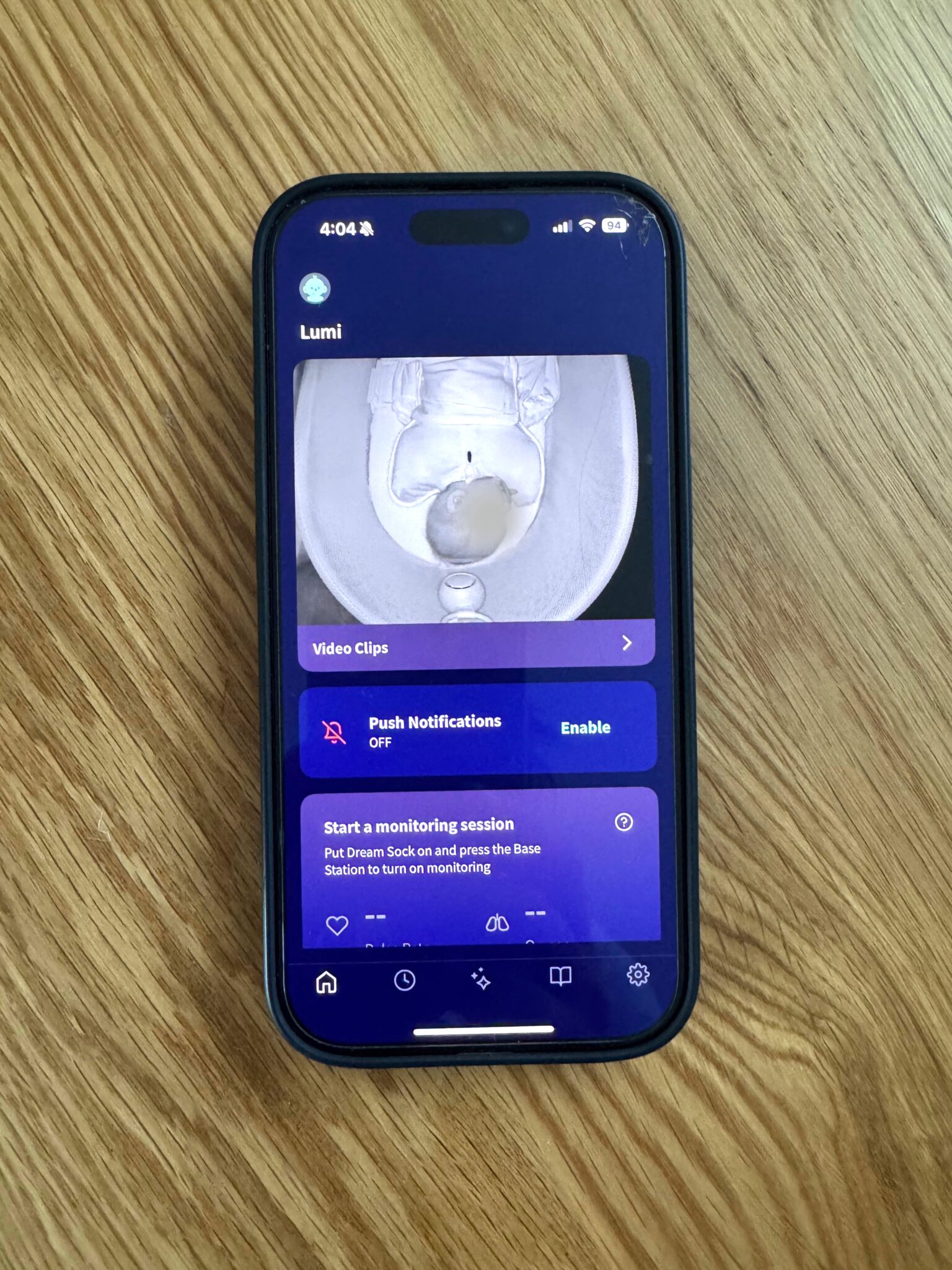 A smartphone displays a baby monitor app showing a live overhead video feed of a baby lying in a crib.