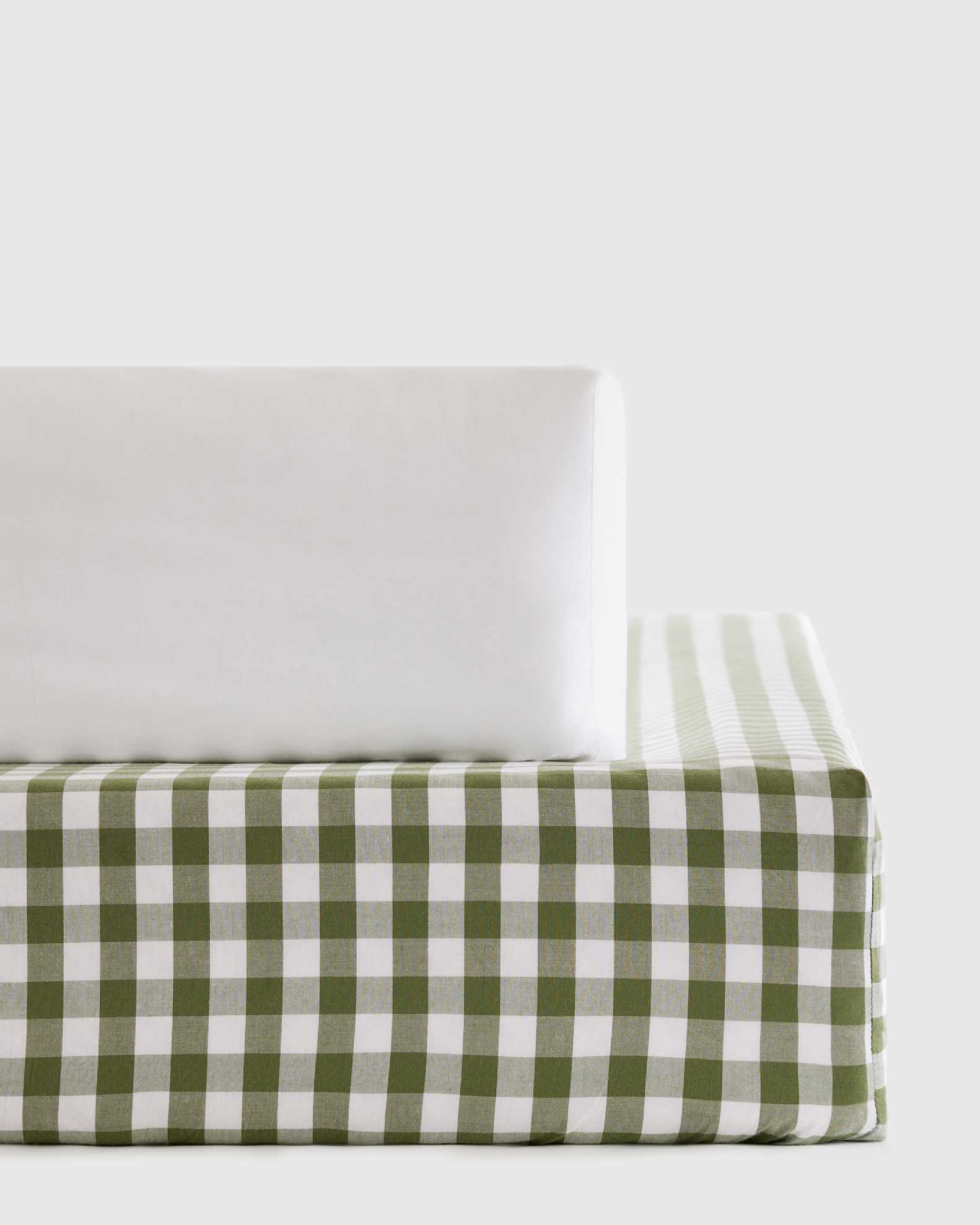 A white pillow rests on a mattress with a green and white checkered pattern against a plain light background.
