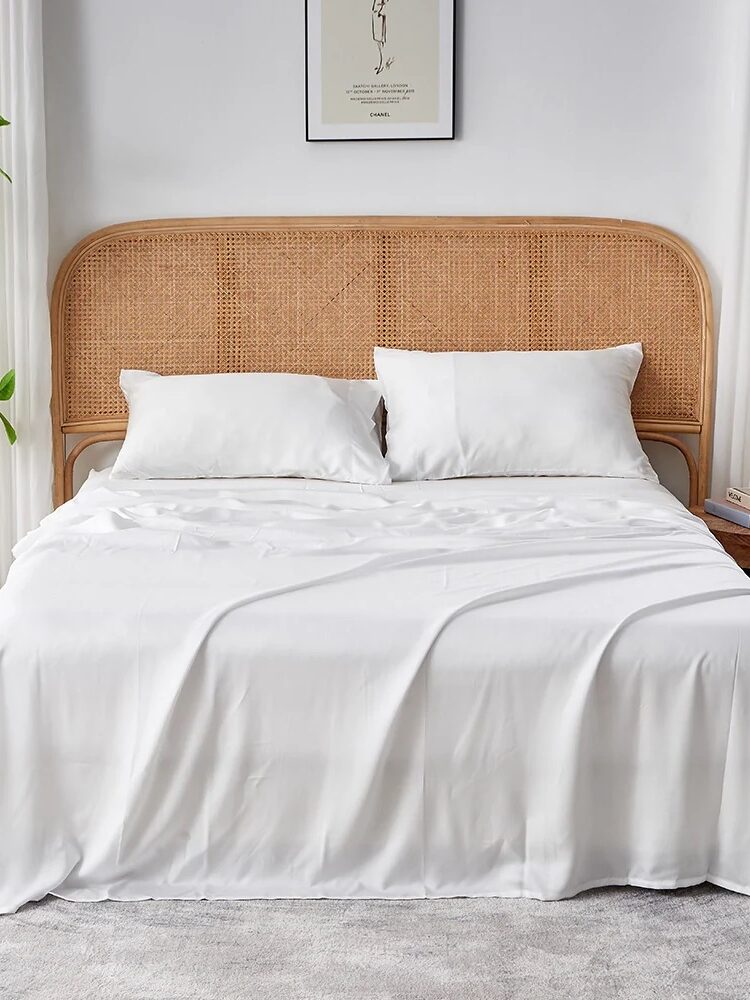 A neatly made bed with white sheets and pillows, a rattan headboard, nightstands, a plant, a lamp, and a framed artwork on the wall in a bright, modern bedroom.