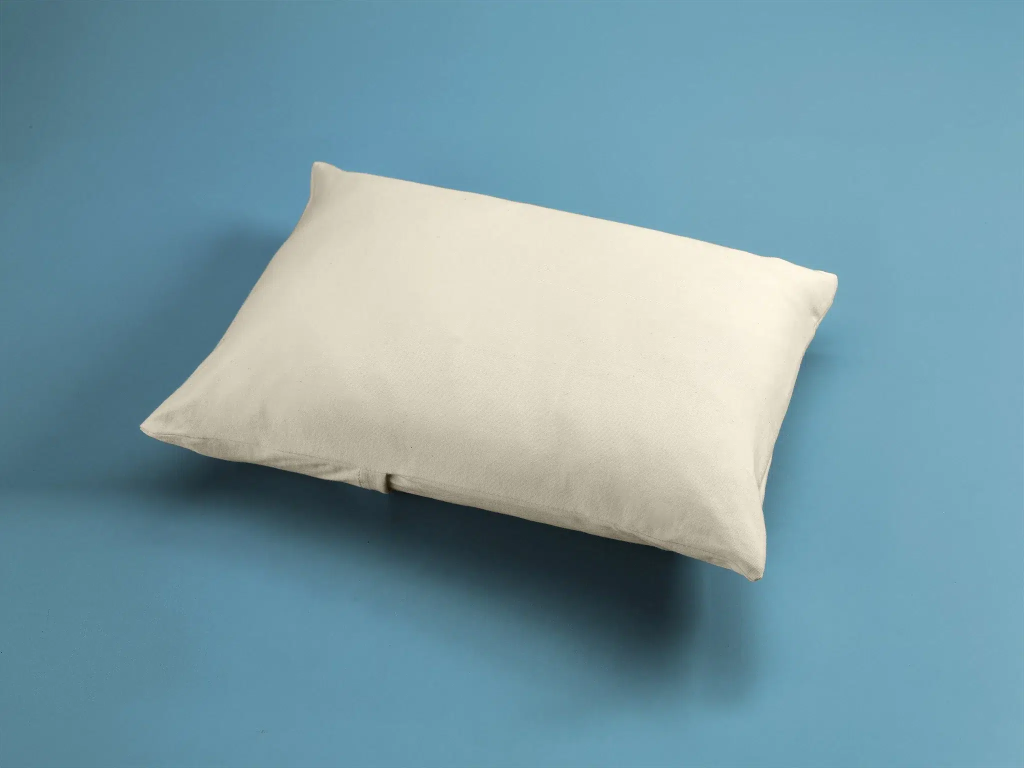 A plain white pillow rests on a solid light blue background.