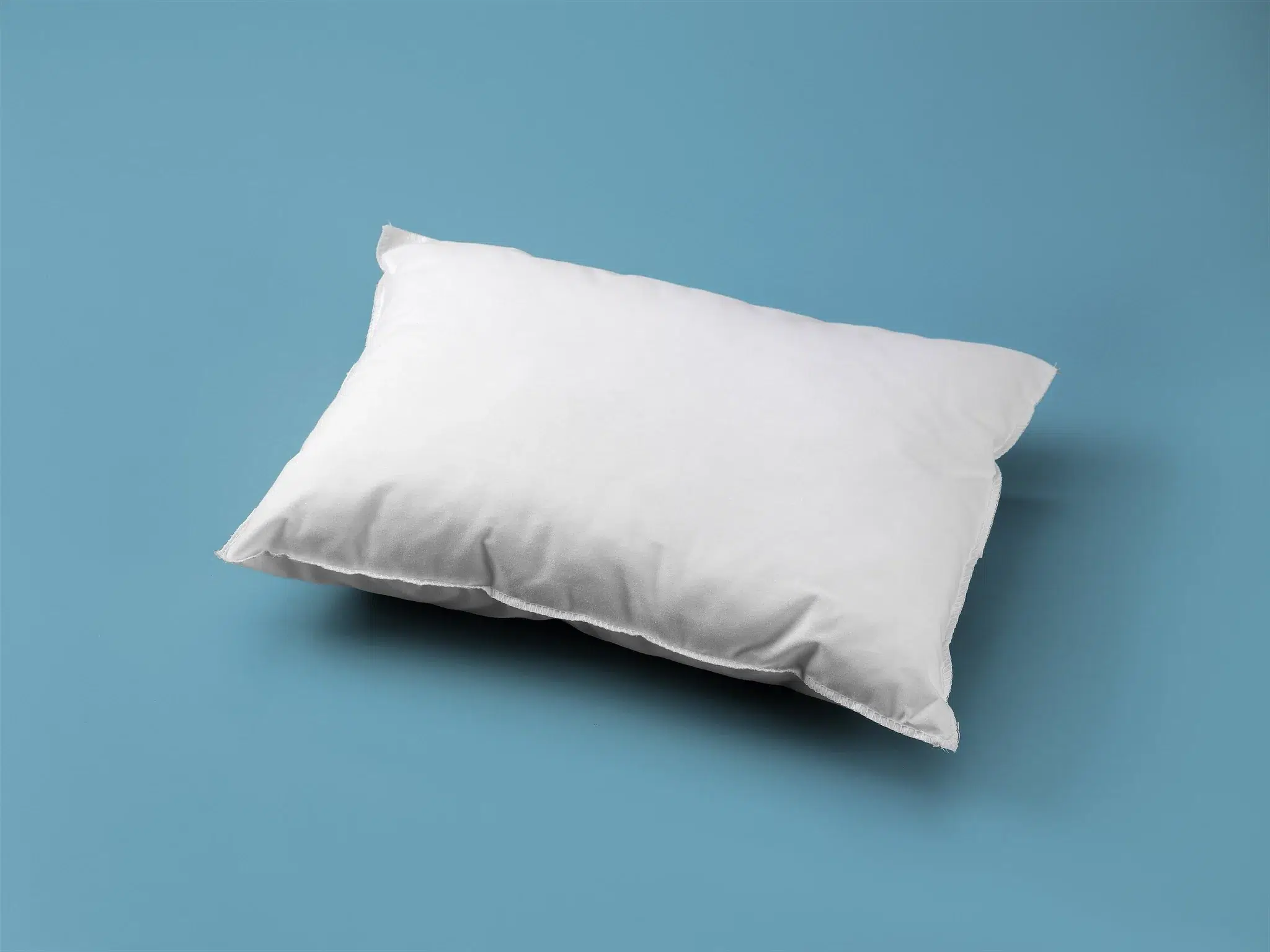 A plain white pillow lies on a flat, light blue surface.