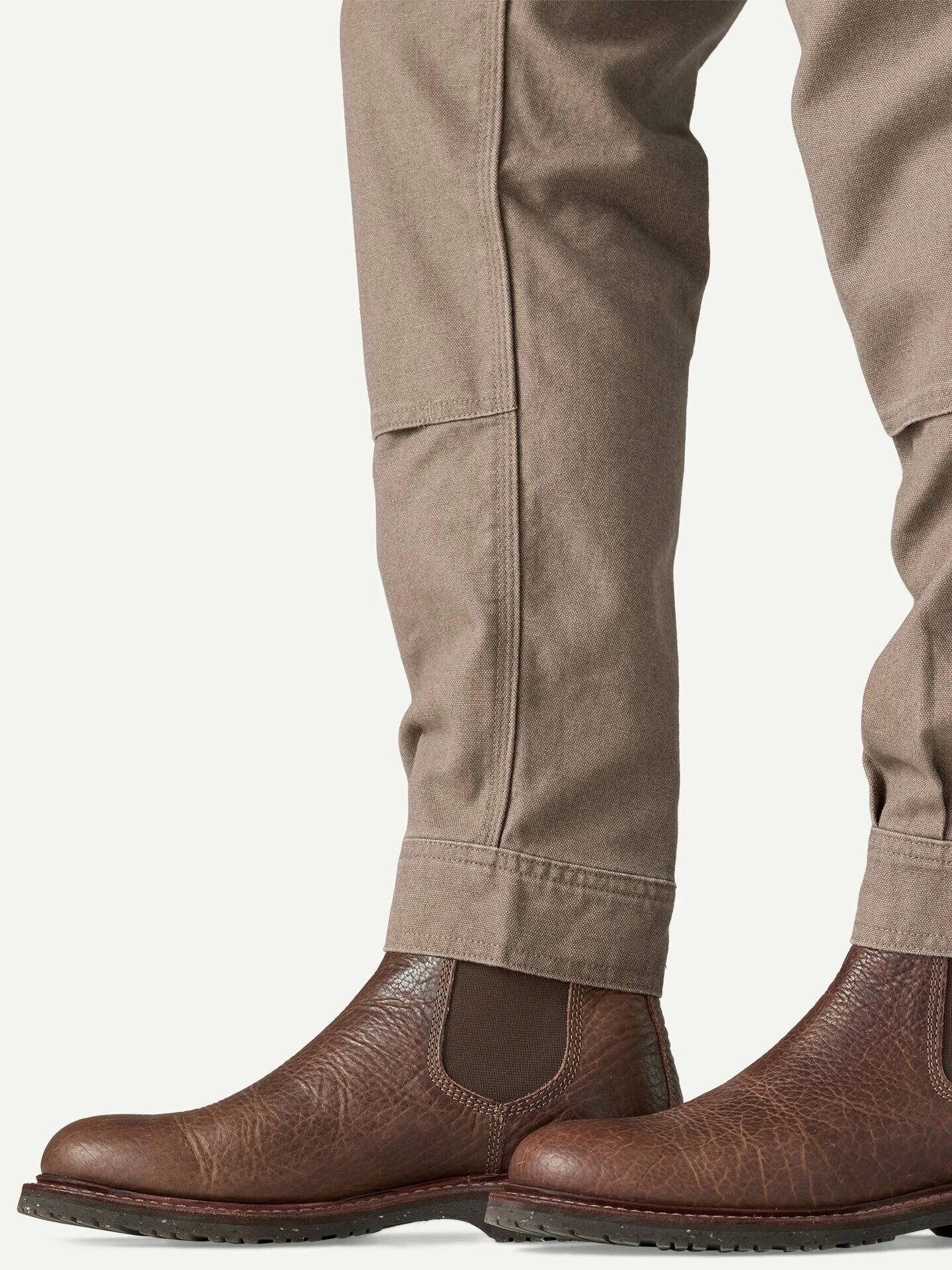 A person wearing light brown pants and brown leather Chelsea boots, shown from the knees down against a plain background.