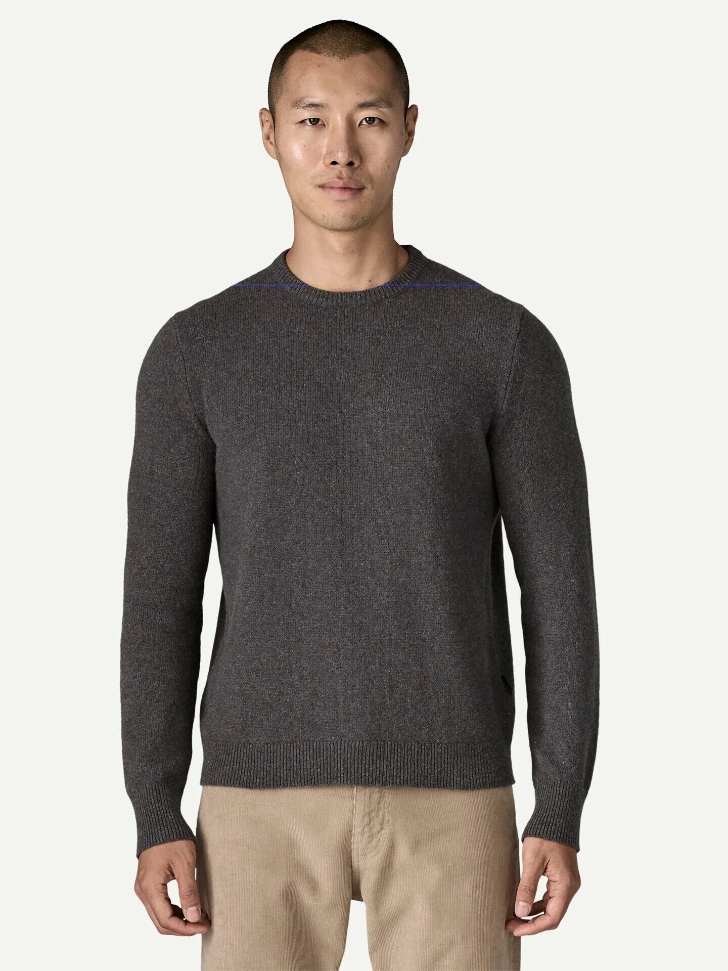 A person wearing a dark gray crewneck sweater and beige pants stands facing forward against a plain light background.