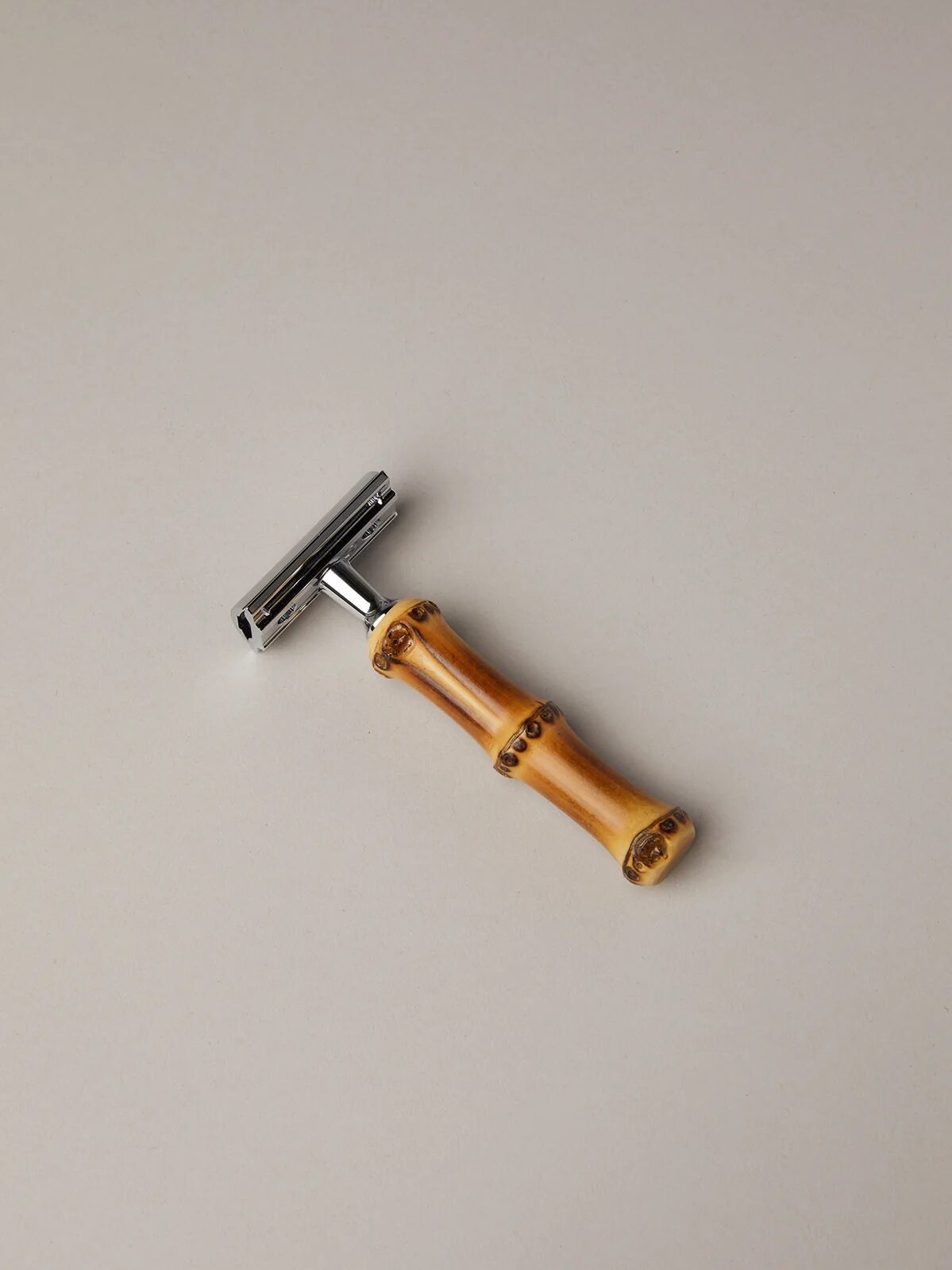 A metal safety razor with a bamboo handle is placed on a plain, light-colored surface.