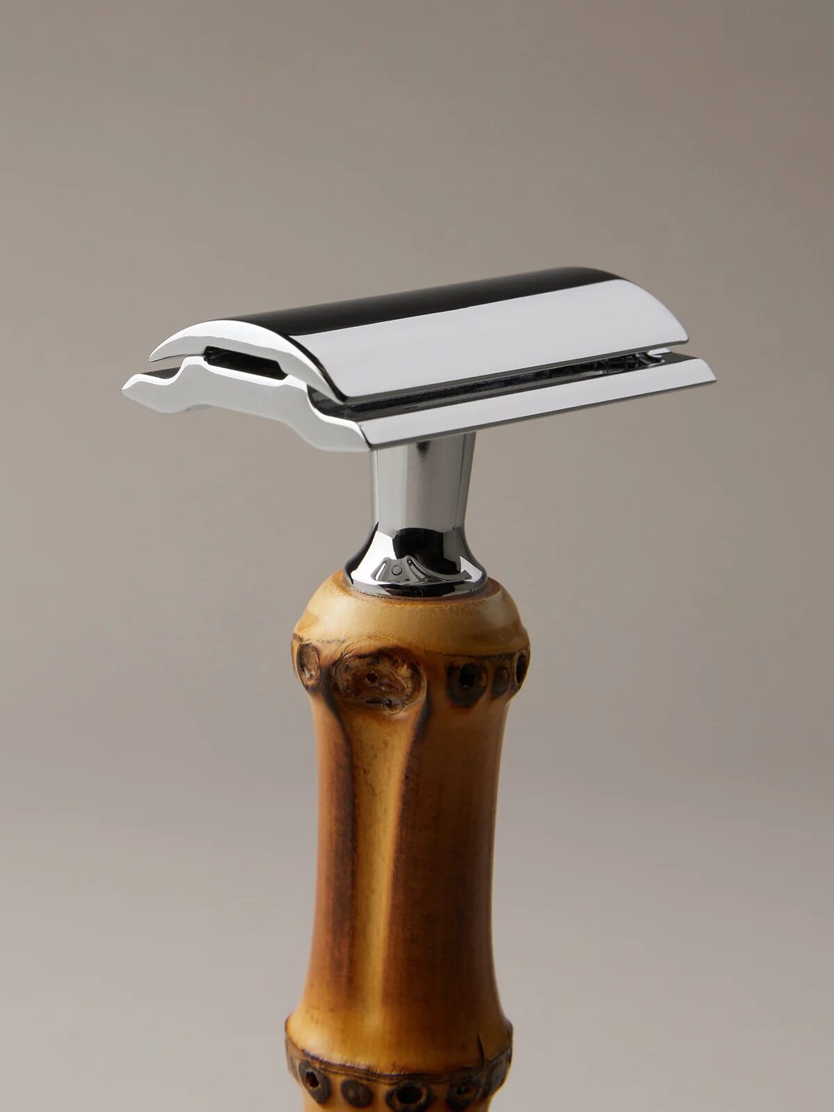 A close-up of a safety razor with a shiny metal head and a brown wooden handle, displayed against a neutral background.