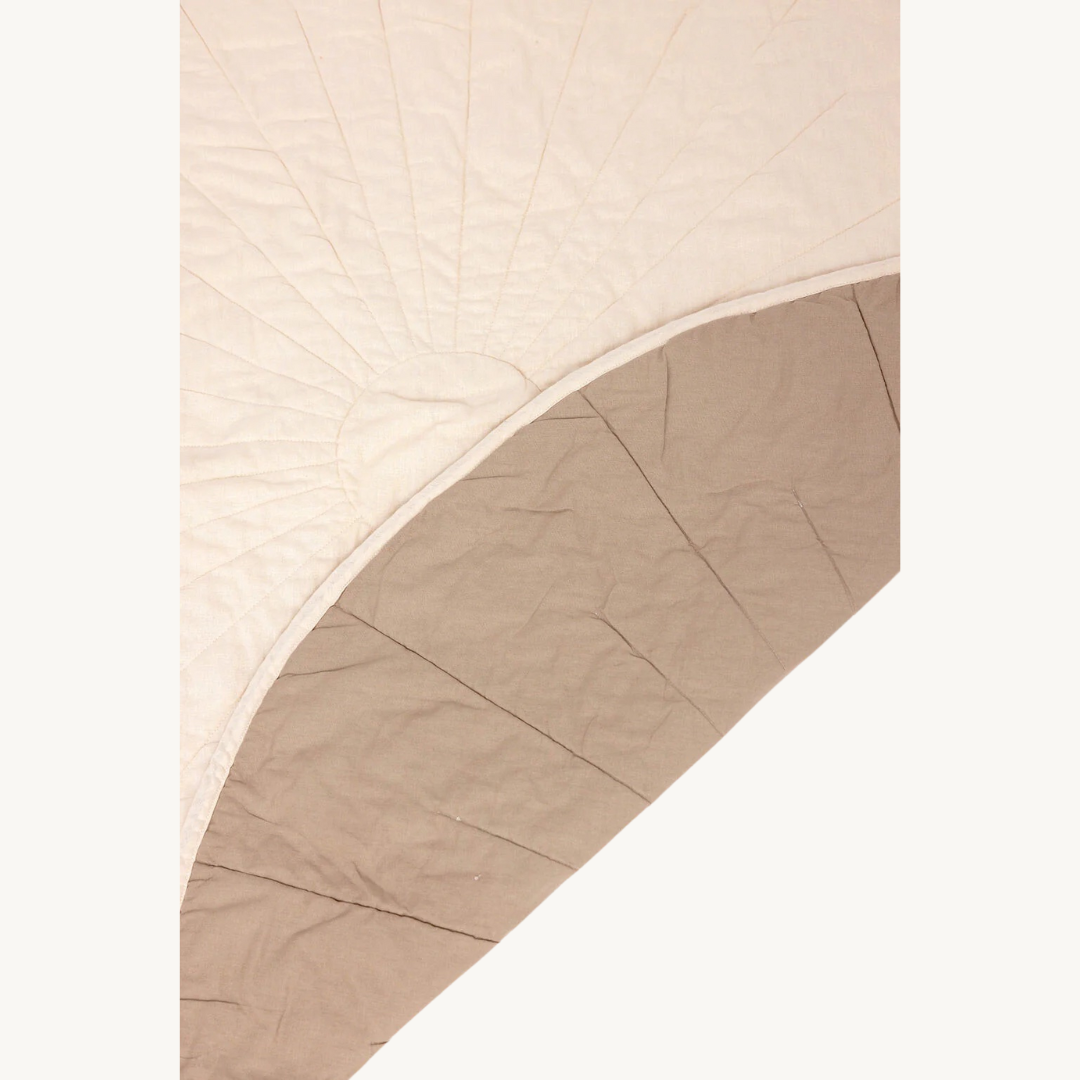 A close-up of a quilt with a sunburst stitching pattern on one side and a solid beige underside, partially folded over to show both sides.