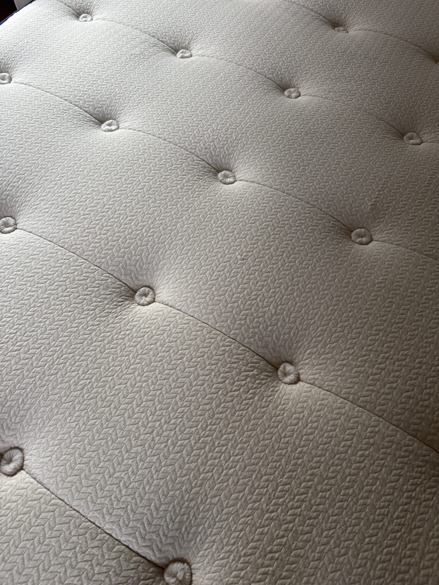 Close-up view of a mattress surface with a textured, patterned fabric and evenly spaced tufted buttons.