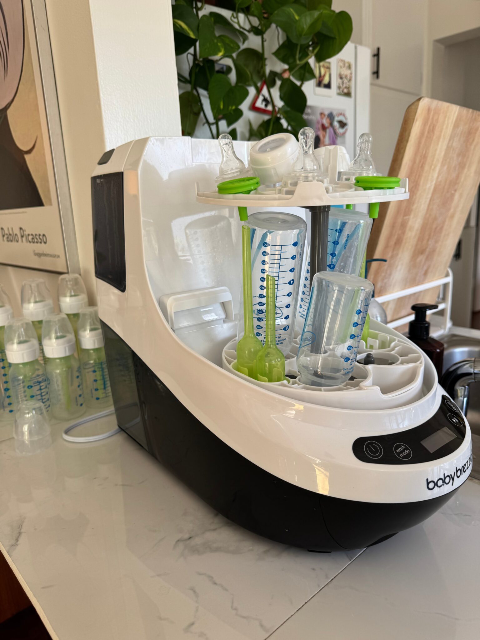 A countertop baby bottle sterilizer holds several bottles and accessories; more clean bottles are drying on the counter nearby.