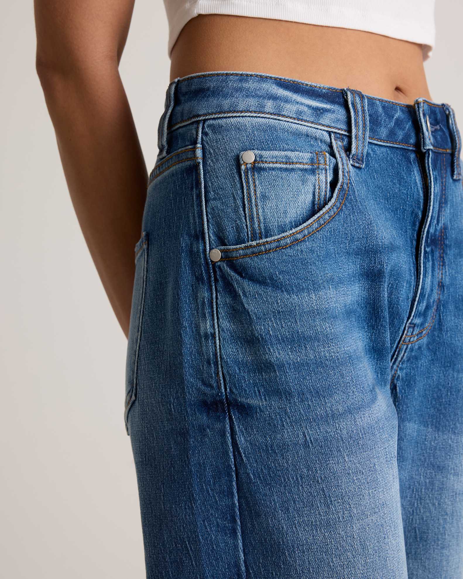 A person wearing high-waisted blue jeans and a white cropped top, shown from the waist to mid-thigh against a neutral background.