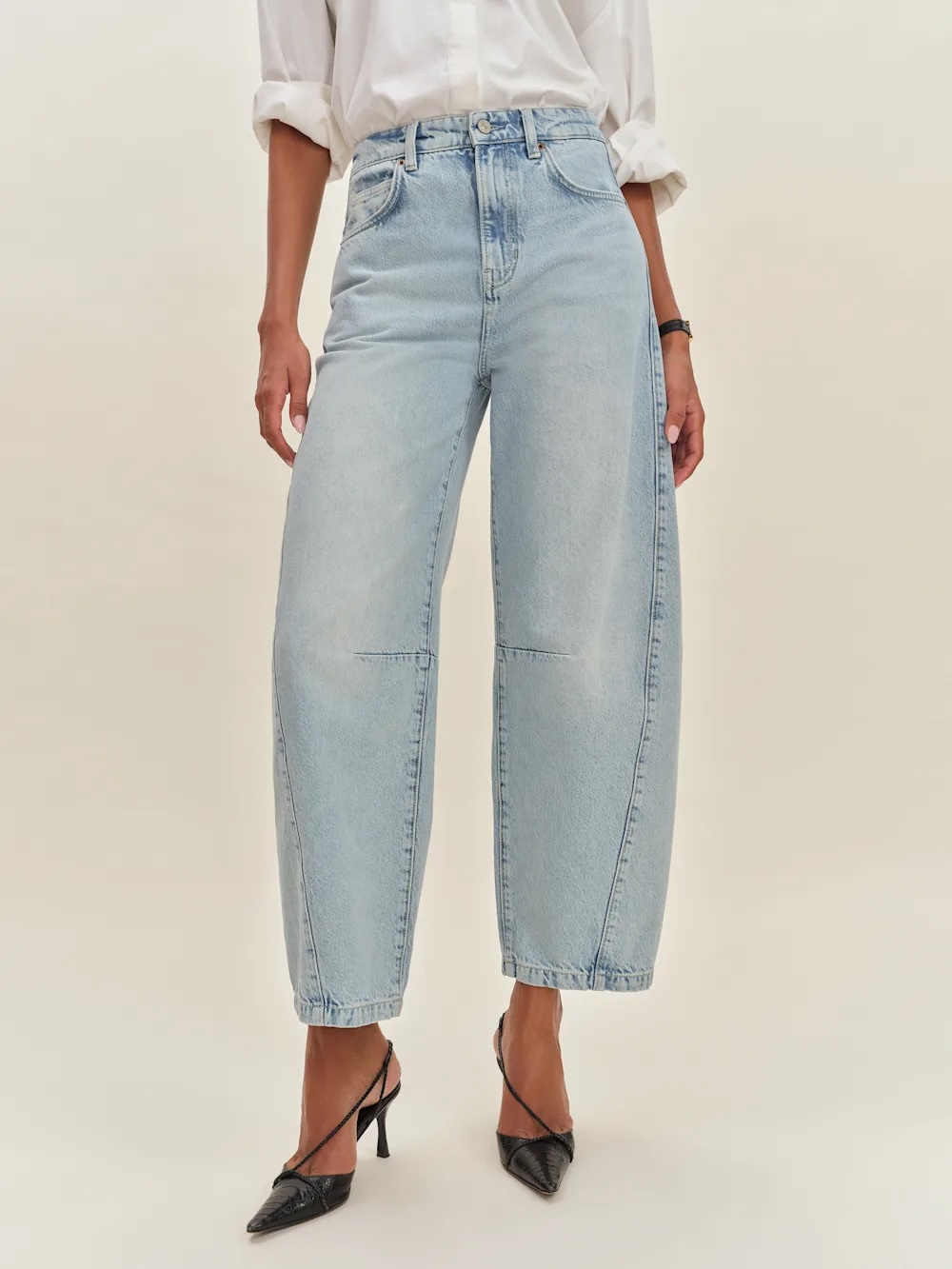 Person wearing light-wash, wide-leg jeans and a white shirt, paired with black pointed-toe heels, photographed against a plain background.