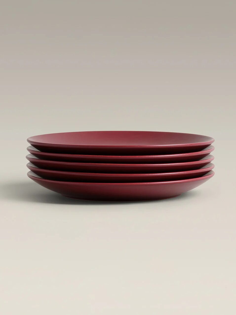 A stack of four maroon ceramic plates arranged neatly on a neutral background.