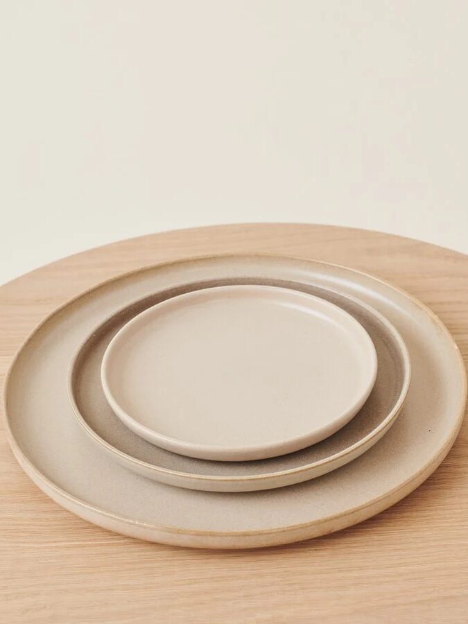 Three stacked ceramic plates of different sizes on a light wooden table with a plain background.