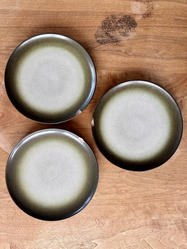 Three round, greenish-gray plates with chipped edges arranged in a triangle on a wooden surface.