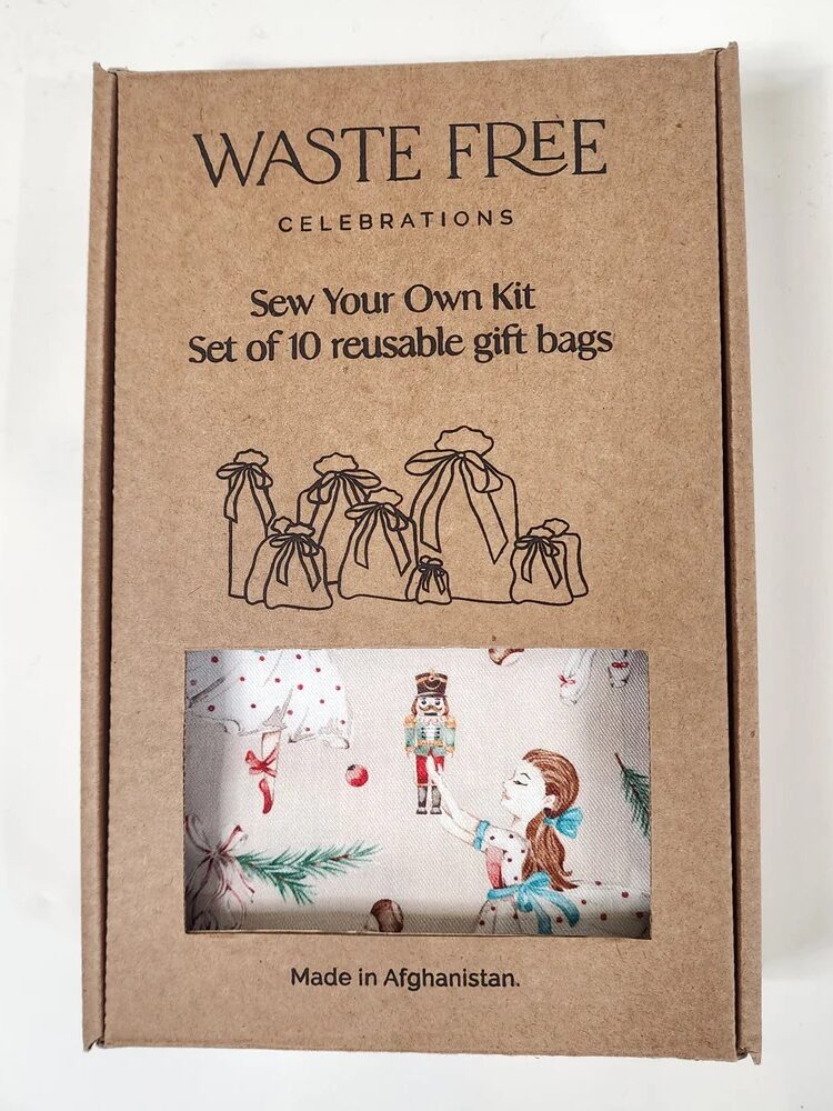 A cardboard box labeled "Waste Free Celebrations" containing a sew-your-own kit for 10 reusable gift bags, with a small window showing printed fabric inside. Text notes it is made in Afghanistan.