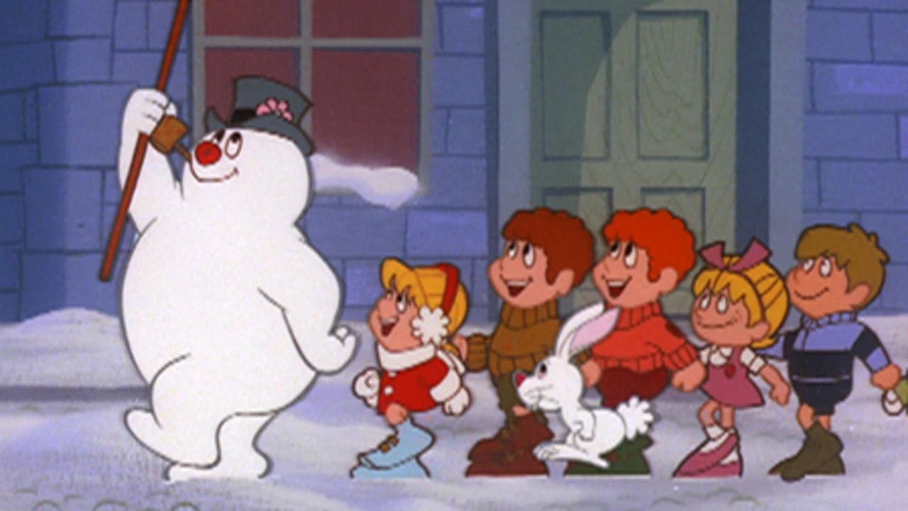 Animated snowman with a black hat and pipe walks in the snow, followed by four children and a white rabbit, in front of a building with windows and a door.