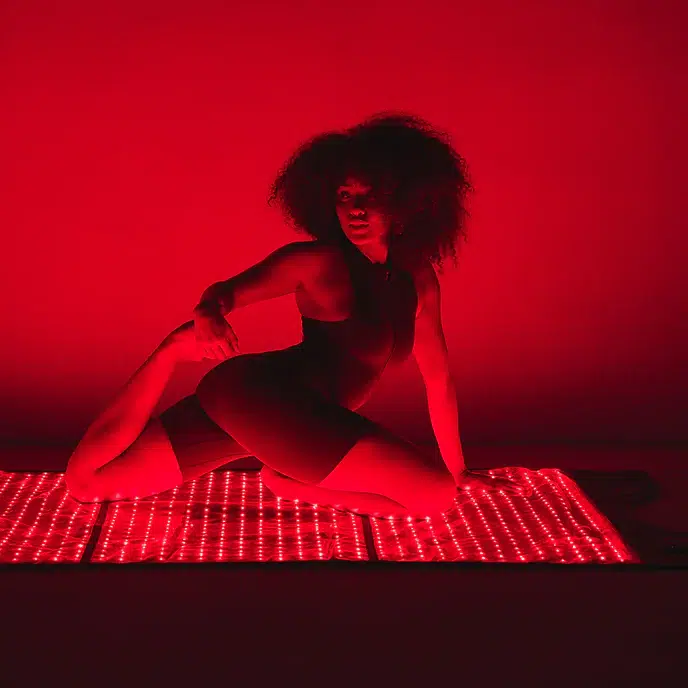 A person in athletic wear poses on a red-lit mat, illuminated by rows of LED lights in a dark space.