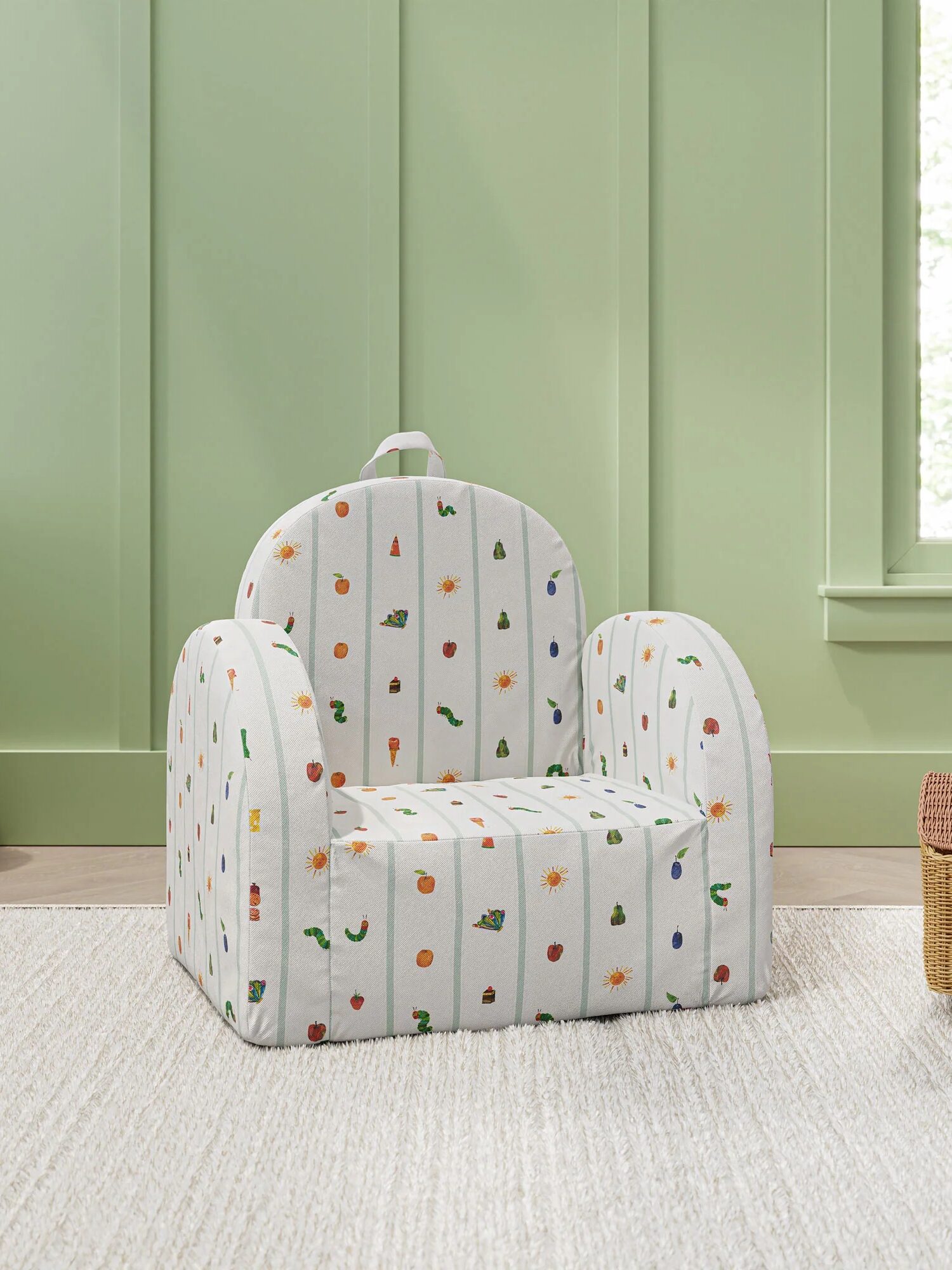 A small upholstered armchair with a whimsical print of colorful vegetables and flowers sits on a light rug against a green paneled wall.