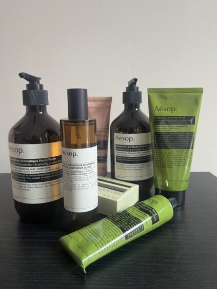 A variety of Aesop skincare products, including hand wash, lotion, body cleanser, body balm, and tubes, displayed on a black surface against a plain light background.