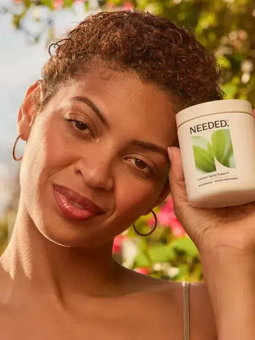A woman holding a Needed supplement container stands outdoors; text beside her lists the product's health benefits, including cellular aging, mitochondrial and ovarian health, and inflammation support.