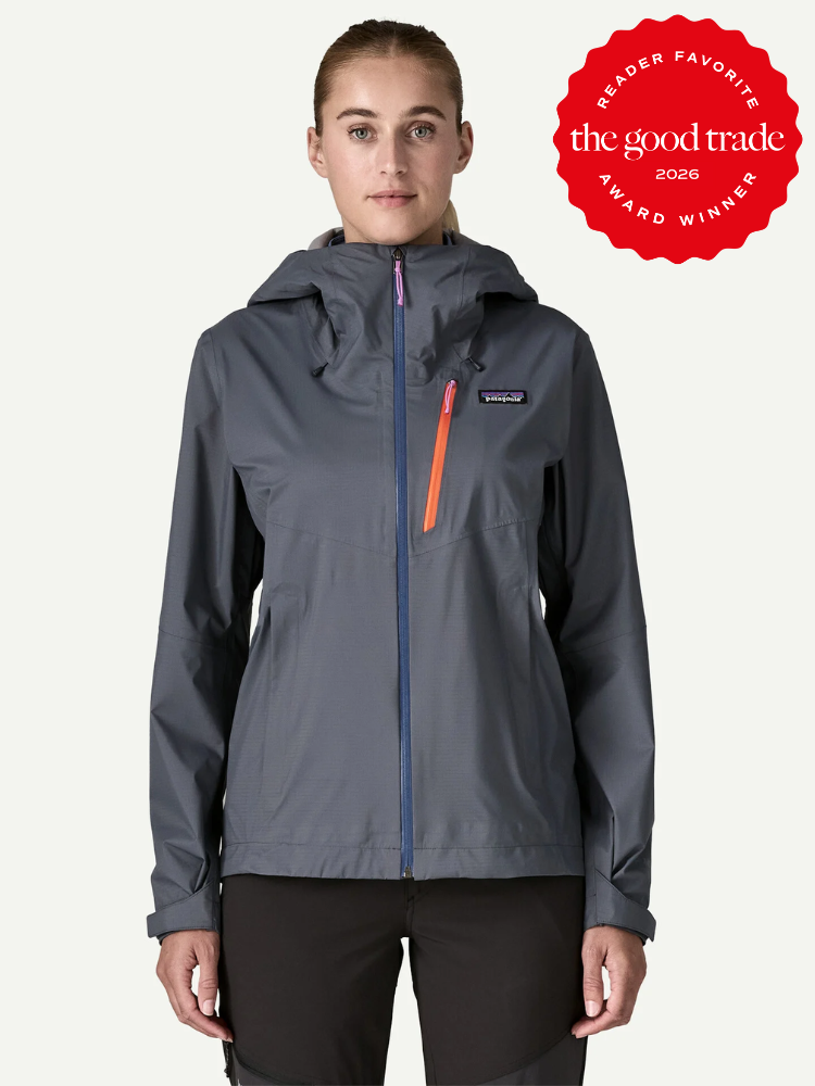 A woman wearing a gray Patagonia waterproof raincoat stands facing forward. A red badge in the corner reads “the good trade reader favorite award winner 2026.”.