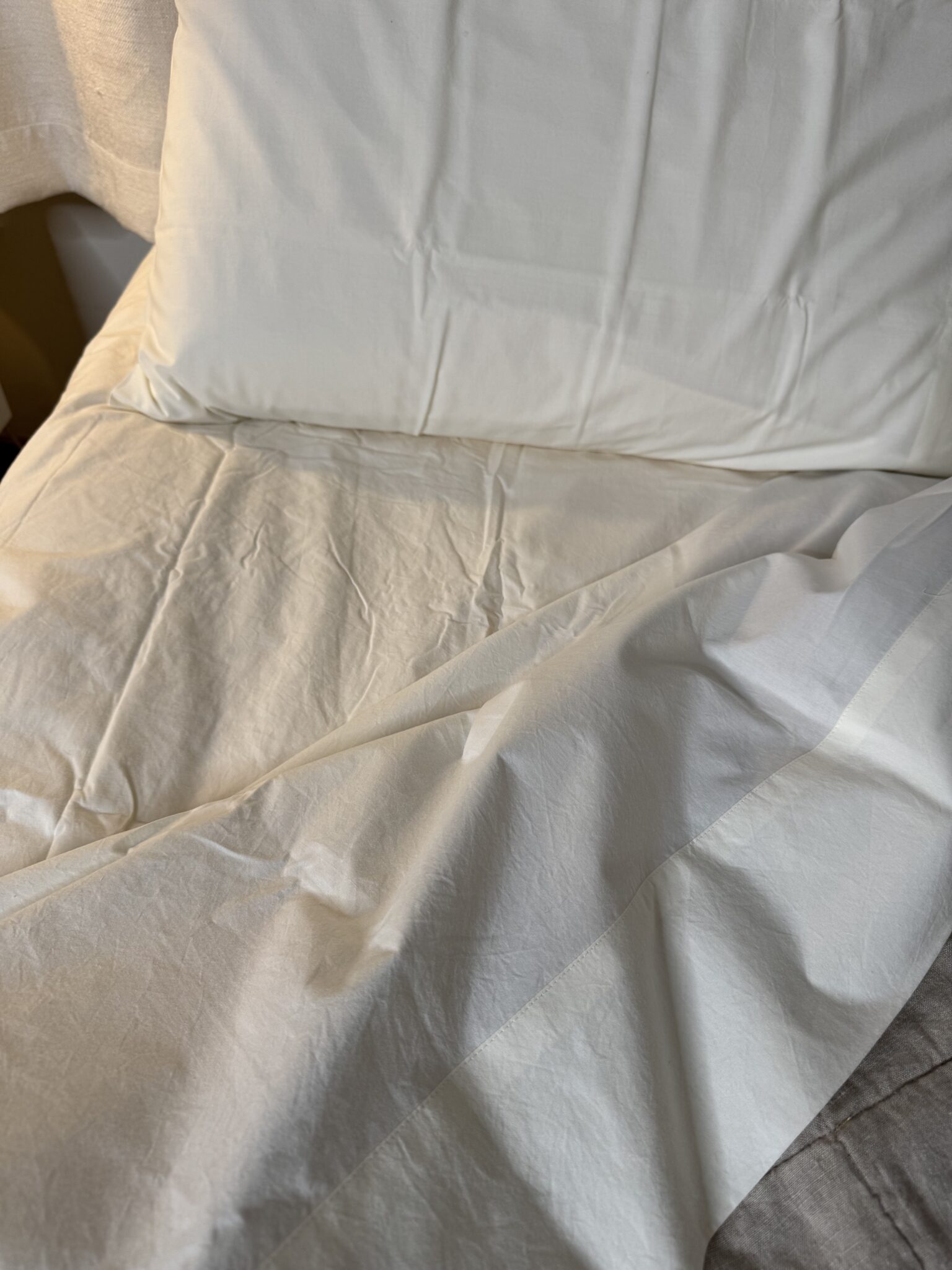 A close-up view of a neatly made bed with white sheets and a pillow.