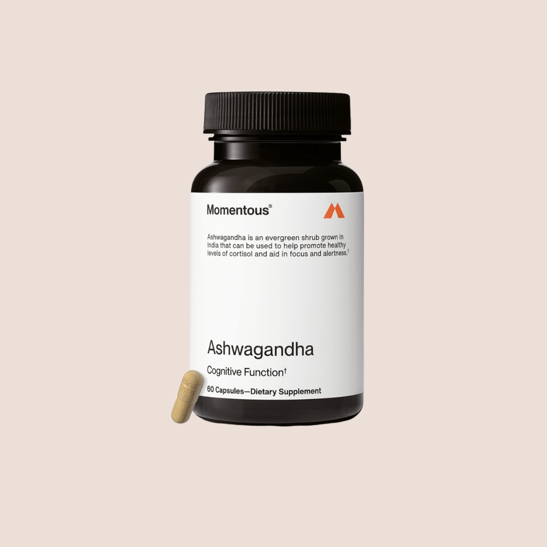 A bottle of Momentous Ashwagandha dietary supplement with 60 capsules and one capsule placed beside the bottle on a light background.