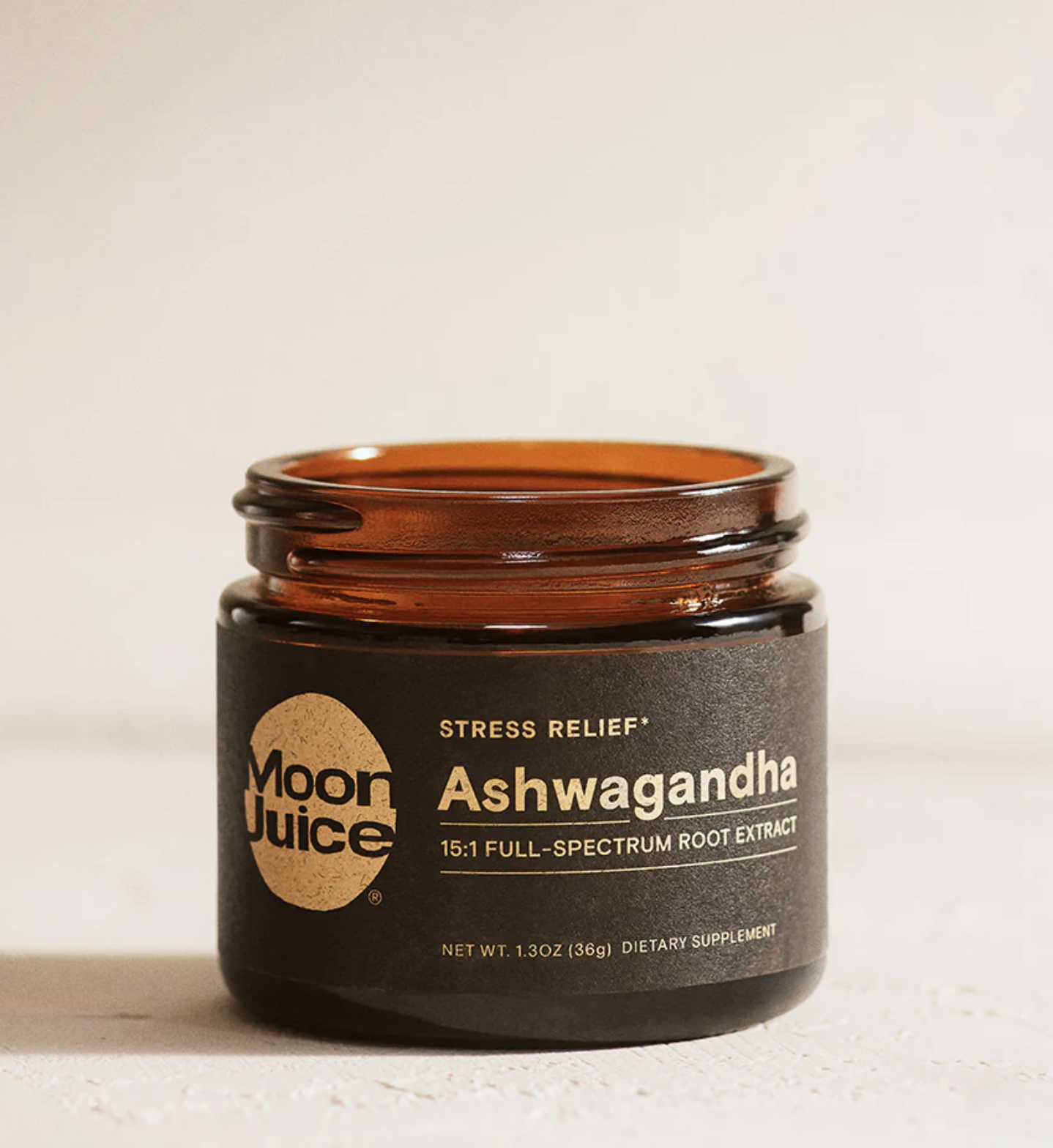 An open brown glass jar labeled “Moon Juice Ashwagandha 15:1 Full-Spectrum Root Extract” is shown on a light surface.