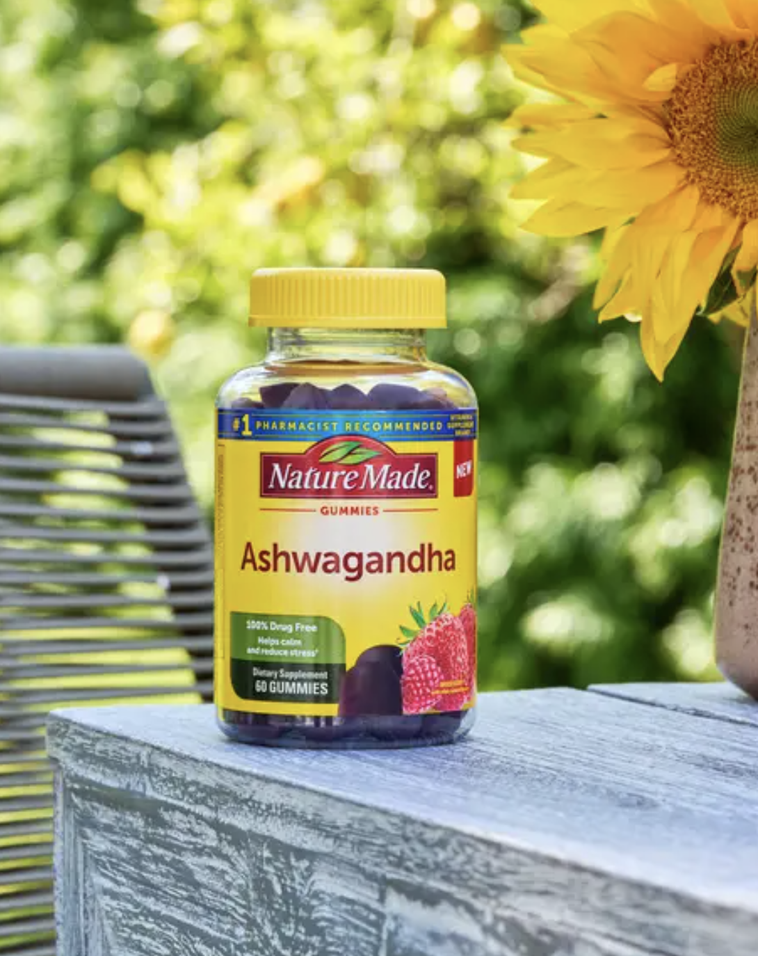 A bottle of Nature Made Ashwagandha gummies sits on a wooden surface outdoors next to a sunflower.
