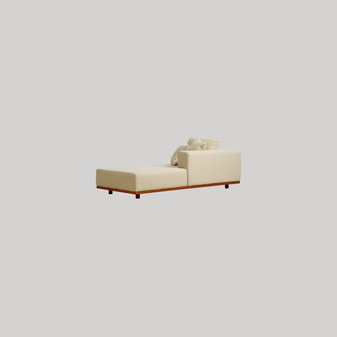 A modern cream-colored chaise lounge with a low wooden base and two matching pillows, set against a plain light gray background.