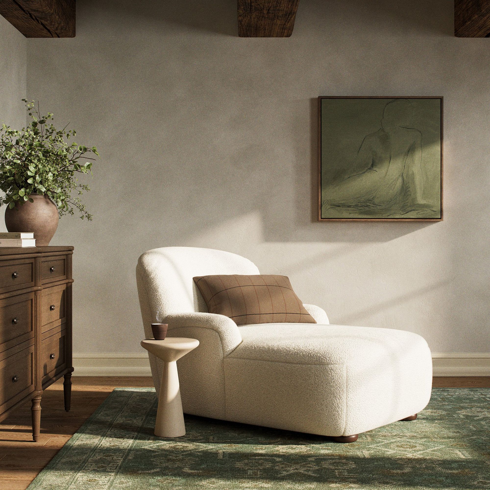 A white chaise lounge with a brown pillow sits next to a small side table in a cozy room with a dresser, potted plant, green rug, and abstract wall art.