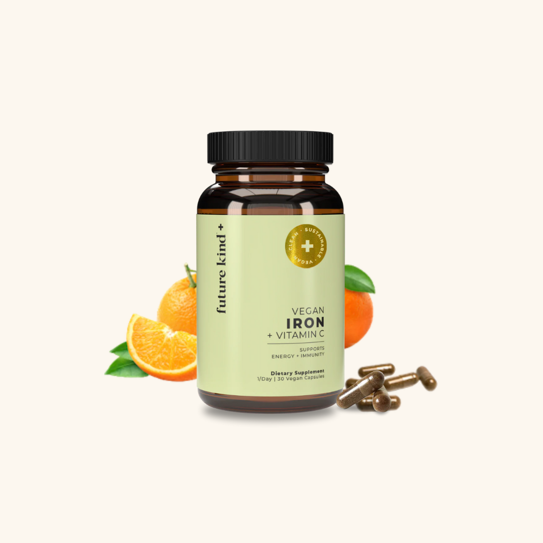 A bottle of Future Kind Vegan Iron + Vitamin C supplement is shown with several brown capsules and fresh orange slices beside it.