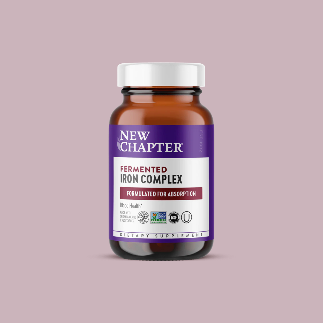 A bottle of New Chapter Fermented Iron Complex dietary supplement with a purple and white label on a light pink background.