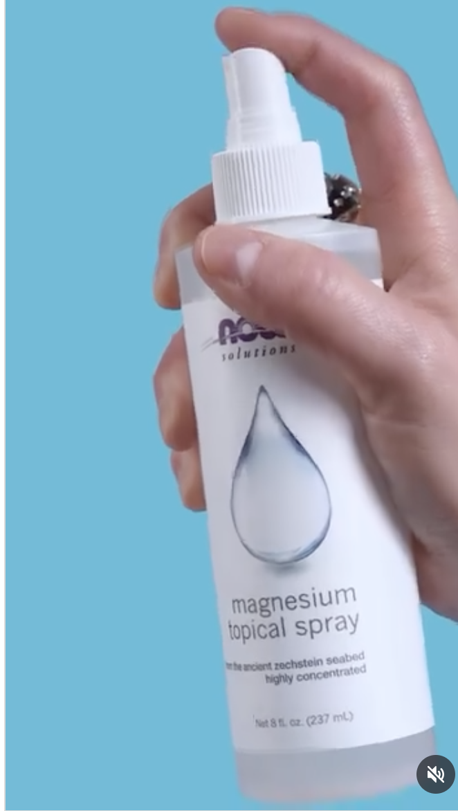 A hand holding a white bottle labeled "magnesium topical spray" with a water droplet graphic against a blue background.