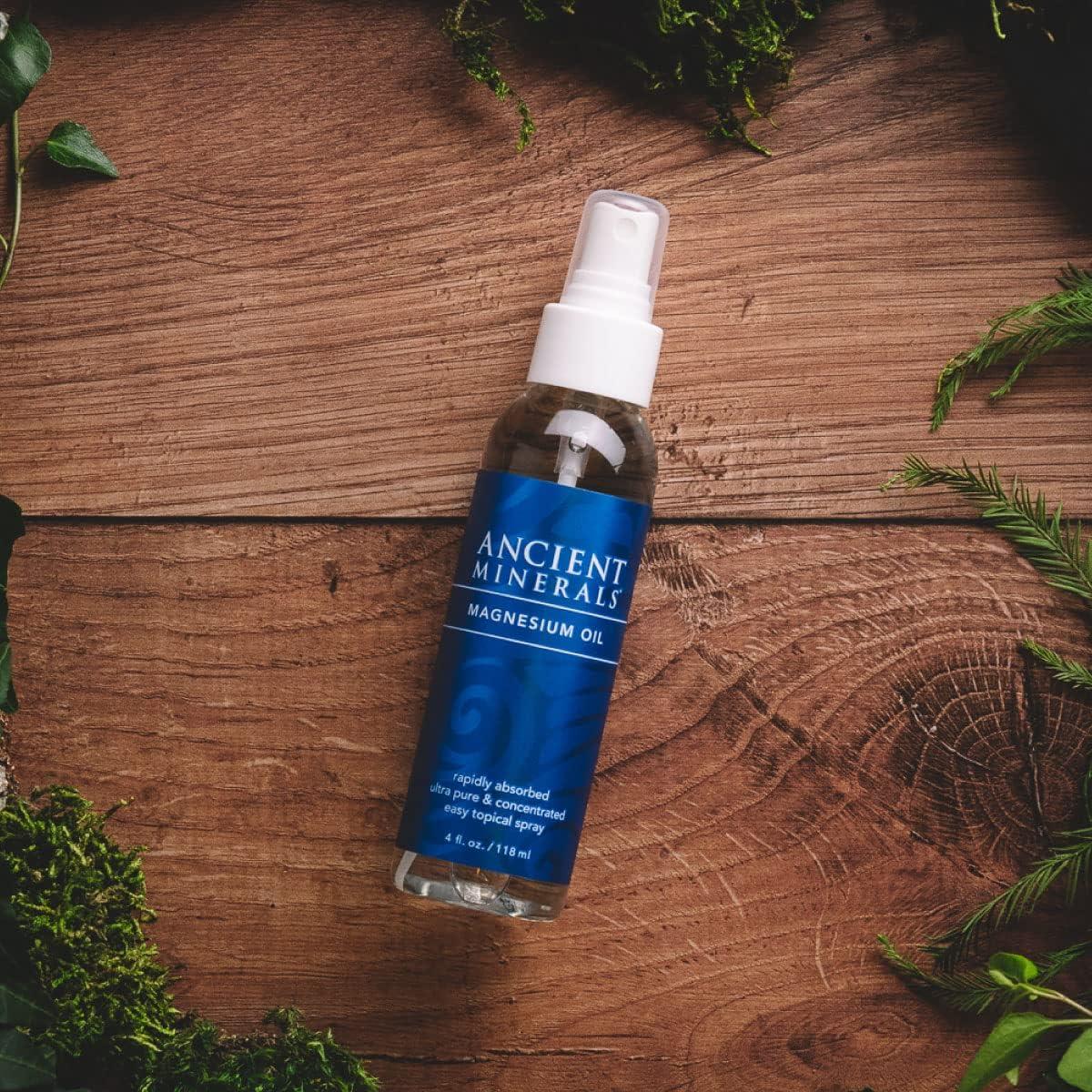 A bottle of Ancient Minerals Magnesium Oil spray lies on a wooden surface surrounded by green foliage.