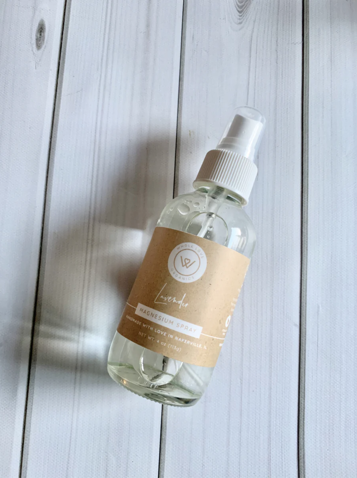 A bottle of magnesium spray with a beige label and white spray cap is placed on a white wooden surface.