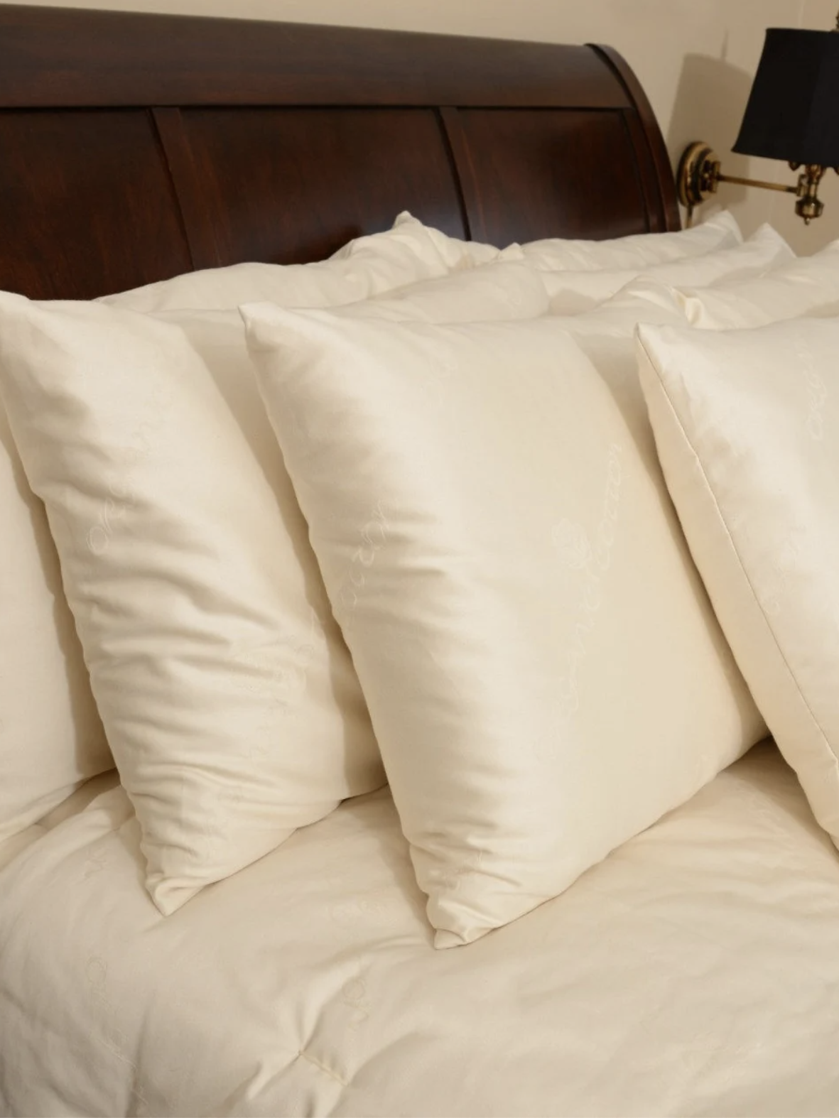 Four white pillows are neatly arranged against the dark wooden headboard of a bed with a cream-colored comforter.