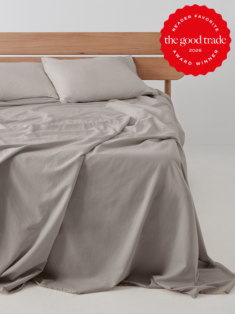 A neatly made bed with light gray cooling sheets and pillows on a wooden headboard; a red “The Good Trade 2026 Award Winner” badge appears in the top right corner.