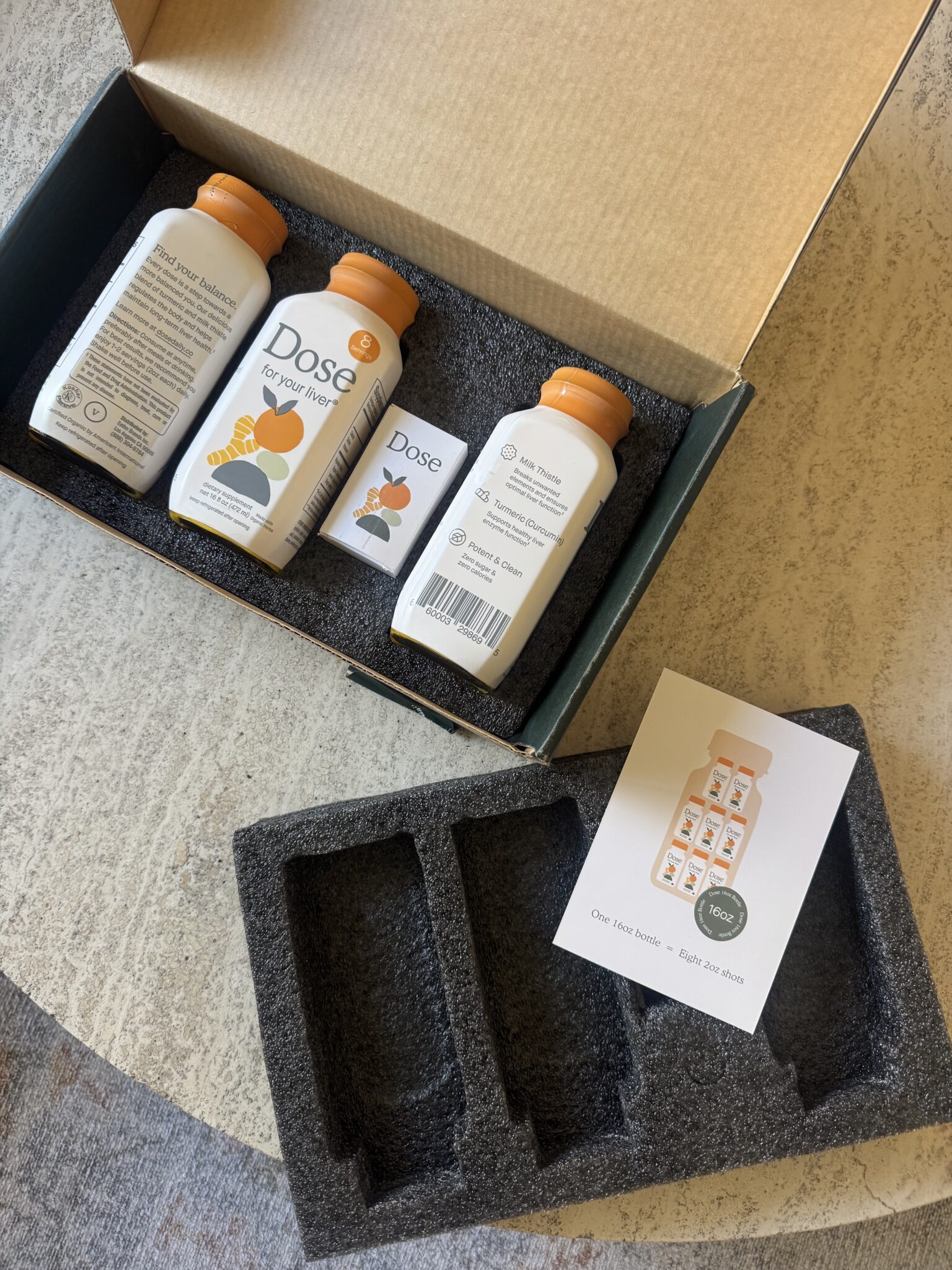 Three bottles of Dose supplement are displayed in a box with foam padding, along with an informational card, on a light-colored textured surface.